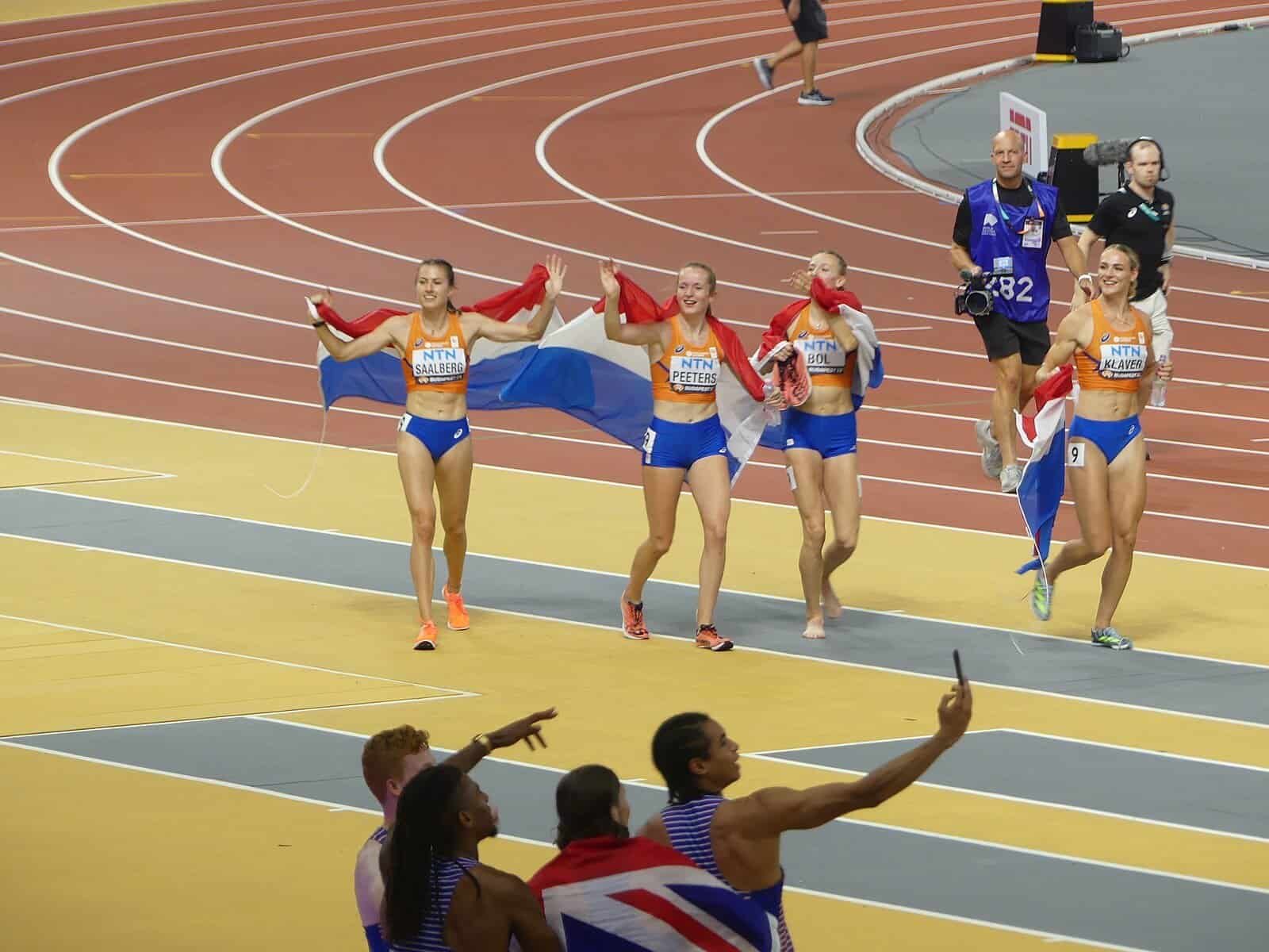 Athletes celebrating on the track in Budapest, a broadcast cameraman behind them and a spectator holding up a phone in the foreground