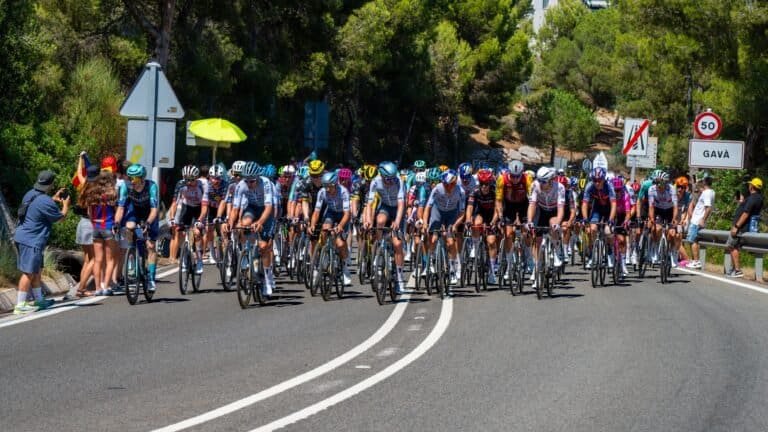 The peloton riding through Gava in Catalonia on a Spanish road race, spectators at the roadside in high summer