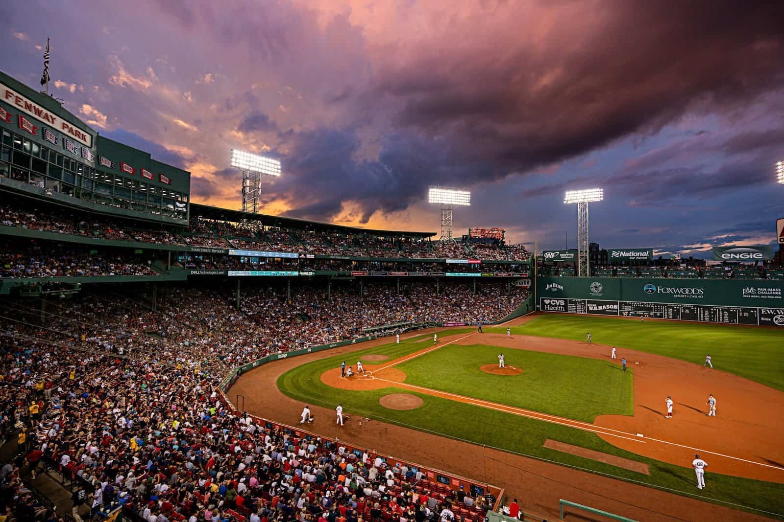 Fenway Park at sunset during a game, with the Green Monster and its scoreboard in left field