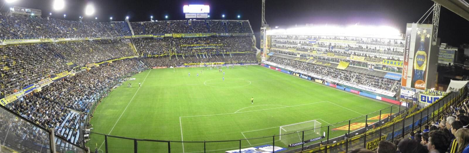 La Bombonera packed at night, showing the steep curved terraces and the flat wall of boxes on the fourth side